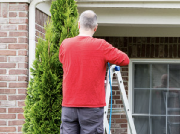 Man standing on ladder in front of his home